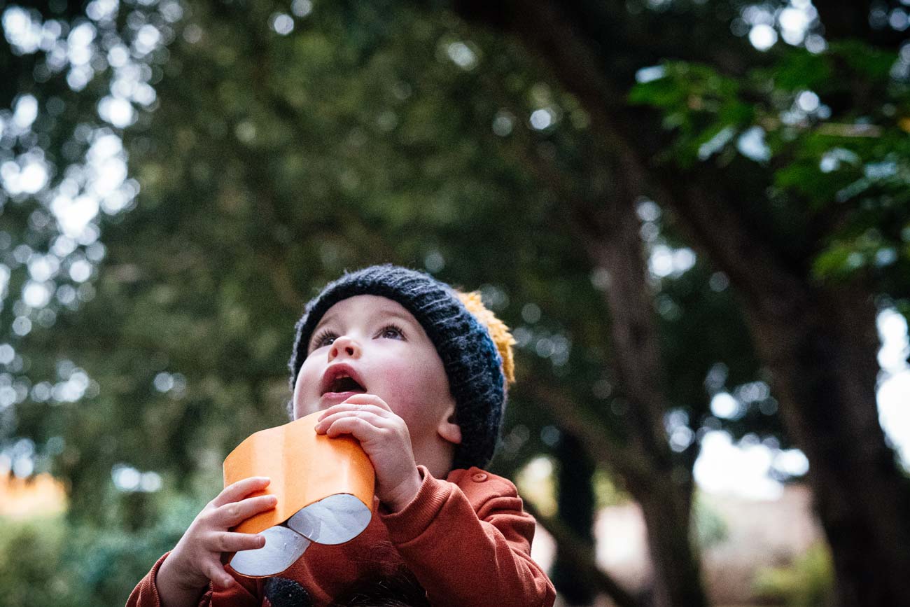 child looks through cardboard binoculars in the woods