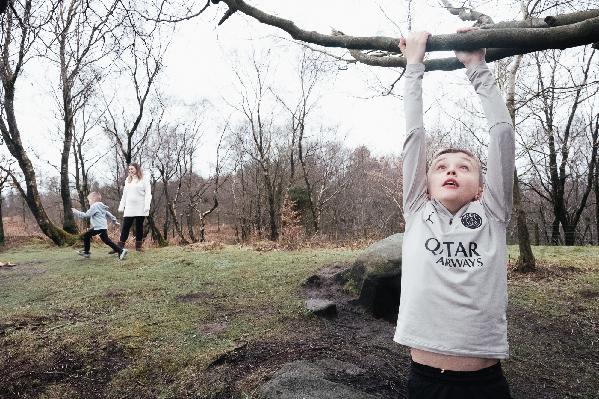 Boy hangs from tree with family in background at Black Rock Derbyshire